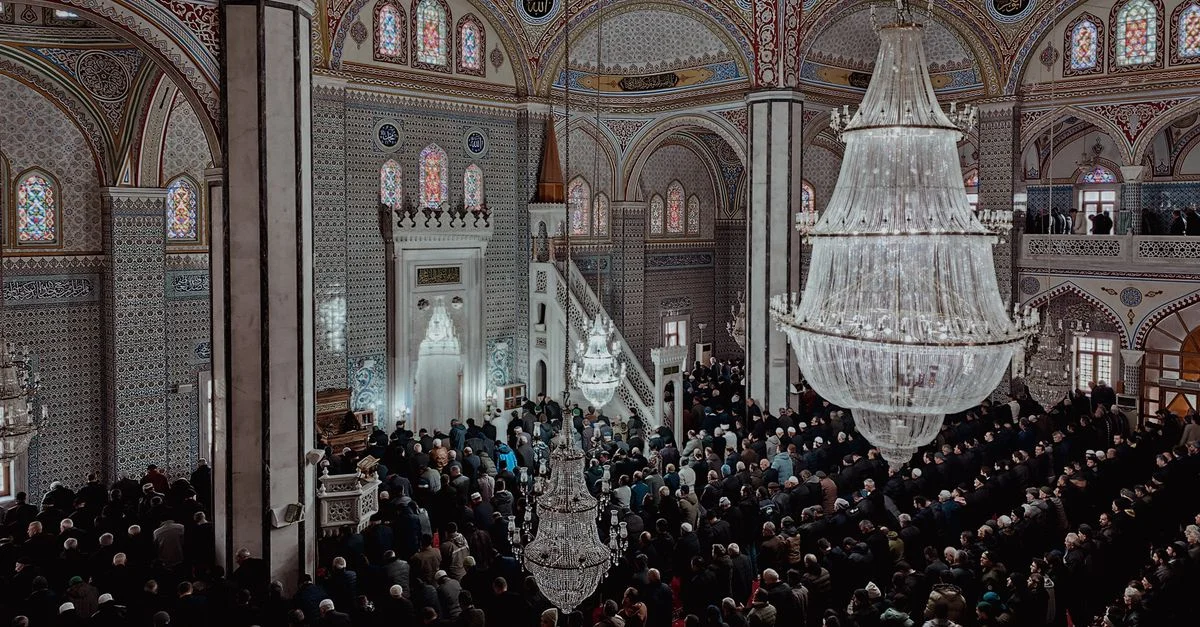 Une grande congrégation se réunit à l'intérieur d'une mosquée magnifiquement décorée sous de grands lustres.