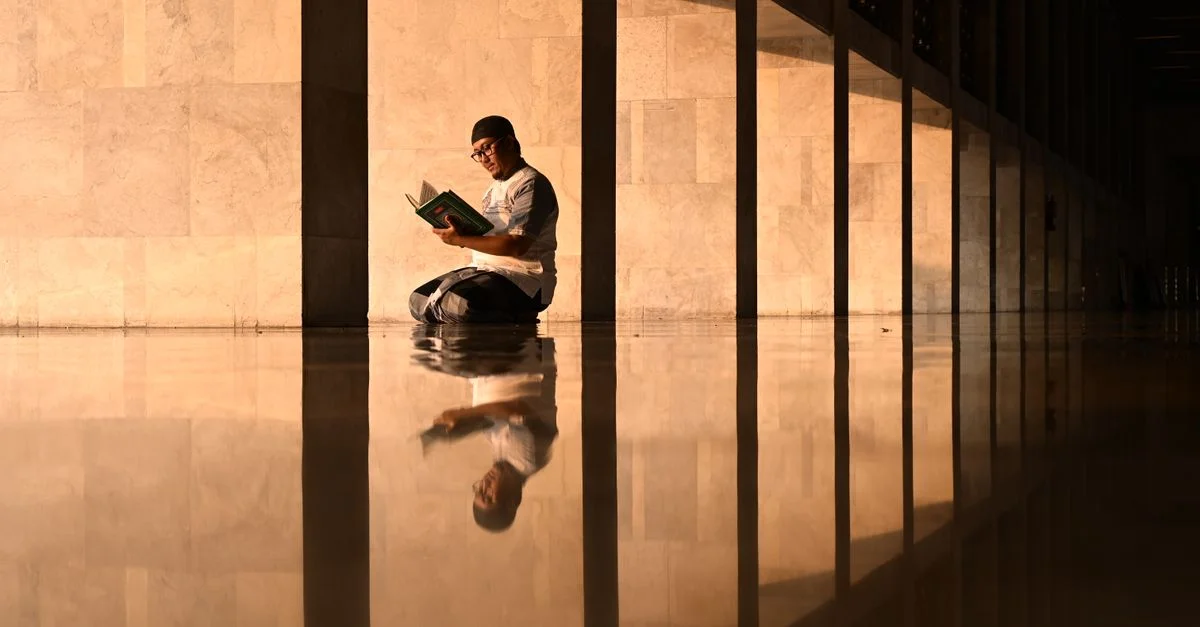 Un homme est assis en train de lire un livre dans un couloir réfléchissant d'une mosquée de Jakarta pendant l'heure dorée.