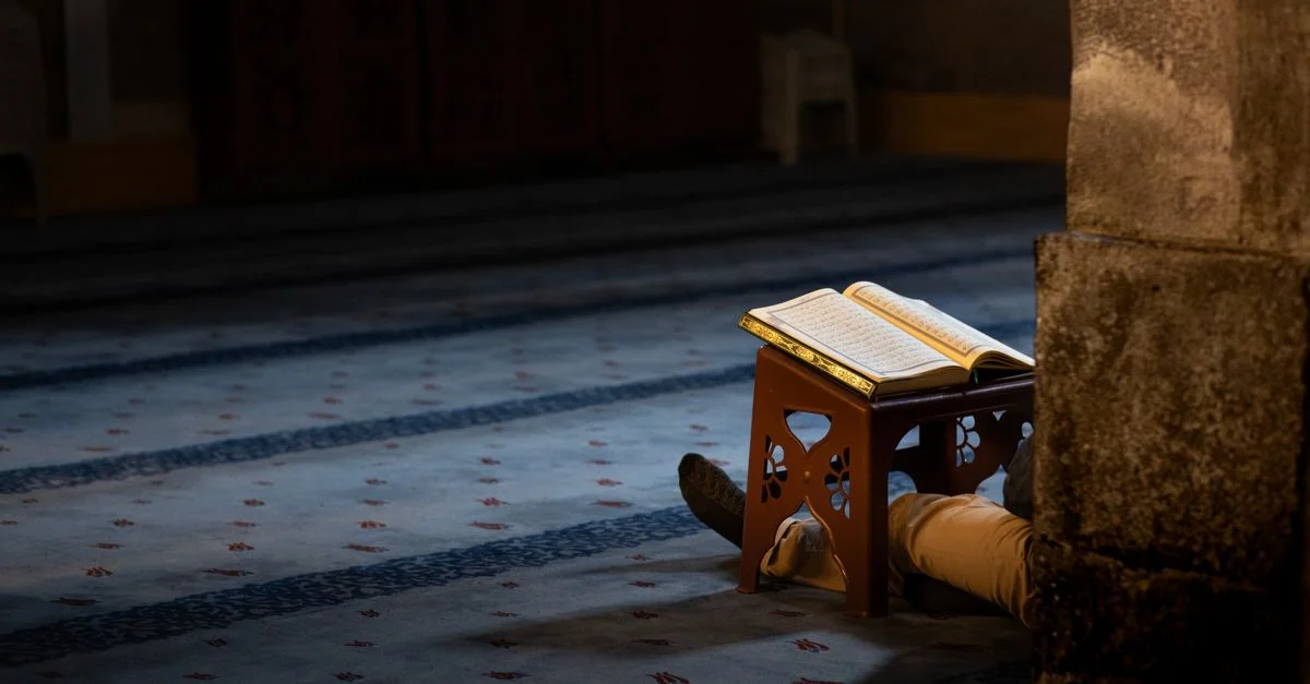 Une personne priant en silence dans une mosquée faiblement éclairée, le Coran ouvert, symbole de paix et de dévotion.